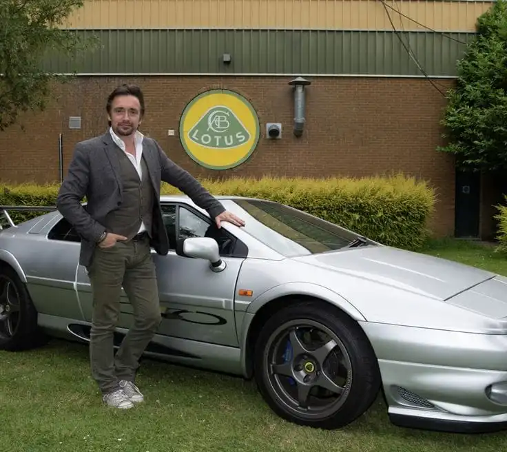 Richard Hammond posing with his Lotus sports car, reflecting his passion for the vehicles that shape his net worth. Richard Hammond standing beside a silver Lotus Esprit outside the Lotus factory — part of the car collection tied to his net worth